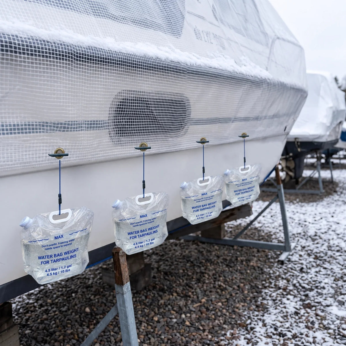 Water bag weights securing a winter tarp on a boat with adjustable bungee cords in snowy conditions.